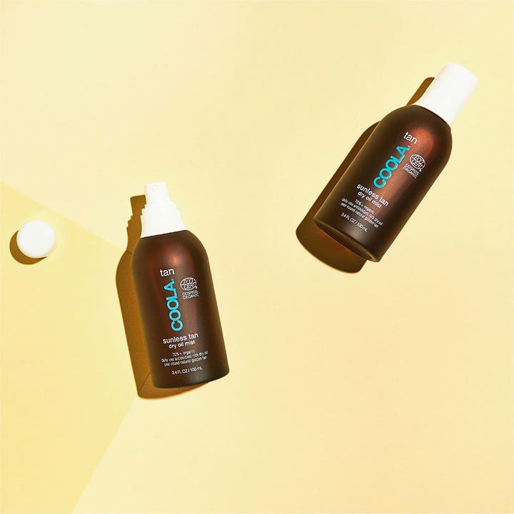 COOLA Sunless Tan Dry Oil Mist 100 ml itsepäivittävä rusketusöljy kahdessa ruskeassa pullossa keltaisella pohjalla.