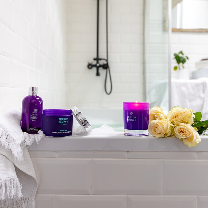 Molton Brown Relaxing Ylang Ylang 300 ml rentouttava suihkugeeli violetissa pullossa kylvyssä keltaisten ruusujen kera