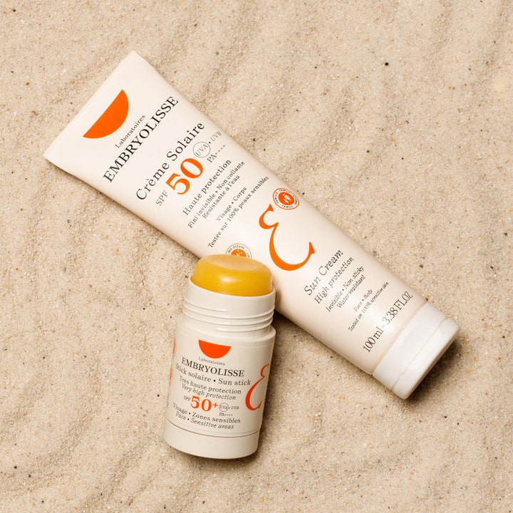 Embryolisse Sun Stick SPF50+ 15 g aurinkosuojapuikko hiekalla keltaisella koostumuksella ja aurinkovoiteella.