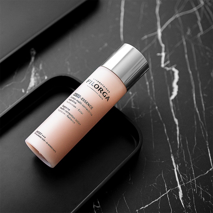 Filorga NCEF-Essence 150 ml heleyttävä hoitoneste vaaleanpunaisessa pullossa mustalla marmorialustalla.