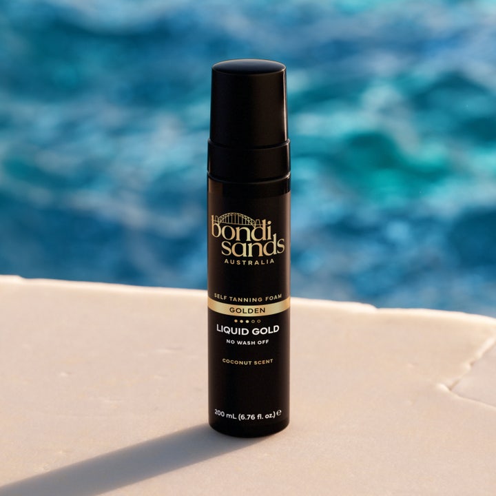 Bondi Sands Liquid Gold Self Tanning Foam 200 ml itseruskettava luo kultaisen hehkun mustassa pullossa uima-altaan äärellä.