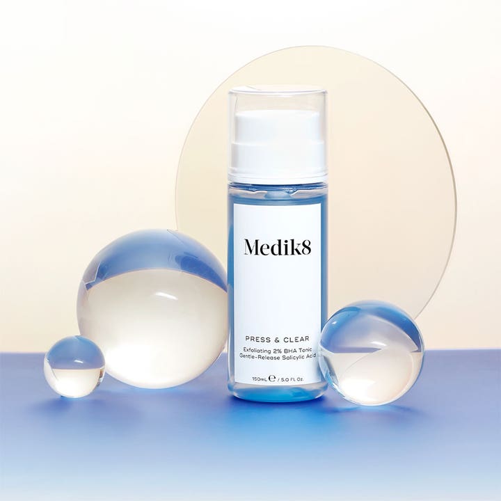 Medik8 Press & Clear 150 ml kuoriva BHA-kasvovesi kirkastaa ihoa, sininen neste kirkkaassa pumppupullossa lasipallojen kera.